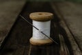 a bobbin with a white thread and a needle stuck into it stands on a wooden table