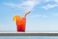 Bocal of fruity cocktail on a beach table. glass of red berry juice with a straw and a slice of orange on wooden table in a bar by Royalty Free Stock Photo