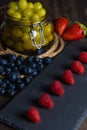 Bodegon fruit, fresh strawberries on slate plate, blueberries and glass jar with fresh grapes on an aged basis Royalty Free Stock Photo