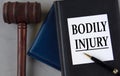 BODILY INJURY - words on a white sheet with leather notebooks, a judge\'s hammer and a pen