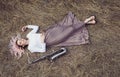 Body of a beautiful young woman in long dress lying on the dry grass next to the saxophone, blonde girl rests on the hay with a Royalty Free Stock Photo