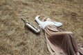 Body of a beautiful young woman in long dress lying on the dry grass next to the saxophone, girl in the summer on the hay rests Royalty Free Stock Photo