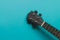 Body of a bright black ukulele guitar against a bright blue back