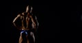 Body brutal bald muscular male bodybuilder closeup on black background, he poses, shows muscles. The view from the back