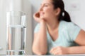 Body Care. Chubby girl sitting at kitchen table looking aside smiling dreamful blurred glass of water close-up Royalty Free Stock Photo