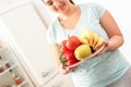 Body Care. Chubby girl standing in kitchen with plate of fruits and vegetables close-up smiling happy blurred