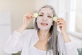 Body and face skin care, anti aging treatment. Close up horizontal shot of pretty senior woman with cloth facial mask Royalty Free Stock Photo