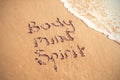 Body mind spirit text written on sand with surf