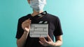 Body part of woman wear face mask and hand`s hold clapper board or movie slate on green mint or Tiffany Blue background Royalty Free Stock Photo