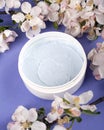 Body scrub in a white jar on a purple background with white flowers apple close-up. skin care, cosmetics, beauty, spa Royalty Free Stock Photo