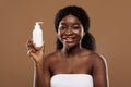 Body Skin Moisturising. Attractive Black Female In Towel Holding Bottle With Lotion Royalty Free Stock Photo