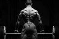 Bodybuilder with great physique and body shape training with barbell in gym over dramatic light