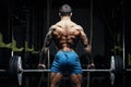 Bodybuilder with great physique and body shape training with barbell in gym over dramatic light Royalty Free Stock Photo