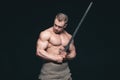 Bodybuilder man posing with a sword isolated on black background. Serious shirtless man demonstrating his mascular body Royalty Free Stock Photo