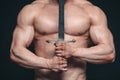 Bodybuilder man posing with a sword isolated on black background. Serious shirtless man demonstrating his mascular body Royalty Free Stock Photo