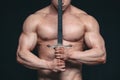 Bodybuilder man posing with a sword isolated on black background. Serious shirtless man demonstrating his mascular body Royalty Free Stock Photo