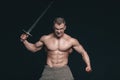 Bodybuilder man posing with a sword isolated on black background. Serious shirtless man demonstrating his mascular body Royalty Free Stock Photo