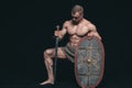 Bodybuilder man posing with a sword and shield isolated on black background. Serious shirtless man demonstrating his Royalty Free Stock Photo