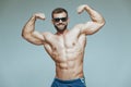 .bodybuilder posing. Beautiful sporty guy male power. Fitness muscled in blue shorts and sunglasses. on isolated grey Royalty Free Stock Photo