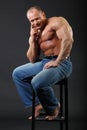 Bodybuilder wearing in jeans sits at stool Royalty Free Stock Photo