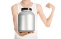 Bodybuilding and Sports theme: a thin man in a white T-shirt and jeans holding a plastic jar with a protein isolated on a white ba