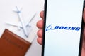 Boeing Airlines app logo on the screen of mobile phone. A blurry image of a plane, a passport and boarding pass on the