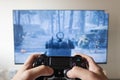 A male hand holding a play station 4 controller with first person shooter video game in a smart tv at background