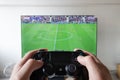 A male hand holding a play station 4 controller with football video game in a smart tv at background