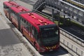 Three wagon transmilenio red bus near to a peatonal bridge of massive transportation system north station on sunny day