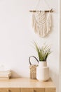 Bohemian concept in stylish interior of living room with flowers in vase, wooden desk, beige macrame, books and elegant.