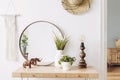 Bohemian concept in stylish interior of living room with flowers in vase, wooden desk, mirror, macrame, books and elegant.