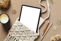 Bohemian feminine workspace with macrame handbag with digital tablet, candle, dried flowers on beige table. Flat lay, top view, Royalty Free Stock Photo