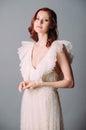 Bohemian wedding, elegant bridal look. Beautiful ginger bride in white wedding dress with sexy decollete and frills on grey backgr