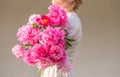 Boho girl holding pink peonies in straw basket. Stylish hipster woman in bohemian floral dress gathering peony flowers on white ba