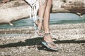 Boho girl wearing jewelry on feet and flip flop sit on dried tree on the beach summer day close up