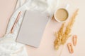 Boho style modern minimal home workspace desk with notebook, cup of coffee, white blanket, dry flowers and feminine accessories.