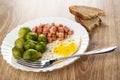 Boiled broccoli, fried egg with cubes of sausage, fork in plate, pieces of bread on wooden table