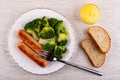 Boiled broccoli with fried sausages in plate, fork, mayonnaise in bowl, bread on table. Top view Royalty Free Stock Photo