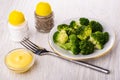 Boiled broccoli in plate, salt, pepper, bowl with mayonnaise, fork on table