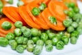 Boiled carrots and grean peas on white plate close up