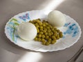 Boiled chicken eggs and canned green peas for easy quick breakfast on a white ceramic plate Royalty Free Stock Photo