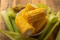 Boiled corn cob in a plate with butter, on wooden textures and green stalks of corn, tasty homemade food, for a picnic Royalty Free Stock Photo