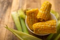 Boiled corn cob in a plate with butter, on wooden textures and green stalks of corn, tasty homemade food, for a picnic Royalty Free Stock Photo