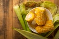 Boiled corn cob in a plate with butter, on wooden textures and green stalks of corn, tasty homemade food, for a picnic, with space Royalty Free Stock Photo
