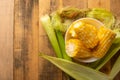 Boiled corn cob in a plate with butter, on wooden textures and green stalks of corn, tasty homemade food, for a picnic, with space Royalty Free Stock Photo