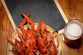 Boiled crawfish, glass of light beer and black chalkboard on a wooden table. Top view picture.