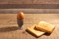 Boiled egg in an egg cup with a slice of fried toast bread on a natural brown wooden background.