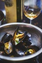 Boiled mussels in shells in a metal saucepan on the stove with a glass of white wine.