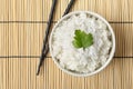 Boiled rice in bowl and chopsticks on bamboo mat, top view Royalty Free Stock Photo