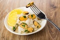 Boiled rice with mussels, lemon, parsley in plate, fork on table